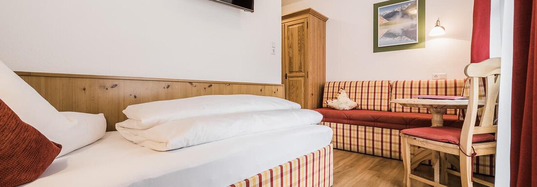 A cozy bedroom with a large bed and a seating area. The decor is bright and inviting, with wooden details and a flat-screen TV. - Andre Arnold - Boutique Hotel - Sölden