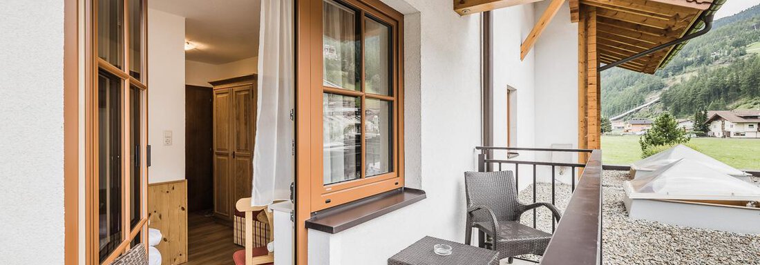 A cozy balcony with two chairs and a table. In the background, mountains and a quiet valley are visible. - Andre Arnold - Boutique Hotel - Sölden