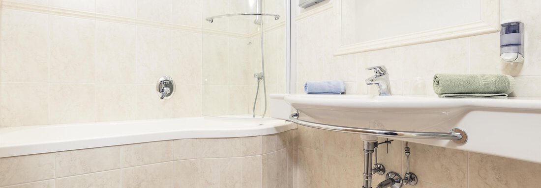 A modern bathroom with a bathtub and a shower. Towels in various colors are placed on the shelf. - Andre Arnold - Boutique Hotel - Sölden