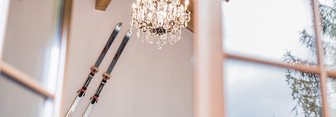 A stylish interior with two skis on the wall and an elegant crystal chandelier. The space has a cozy, modern character. - Andre Arnold - Boutique Hotel - Sölden