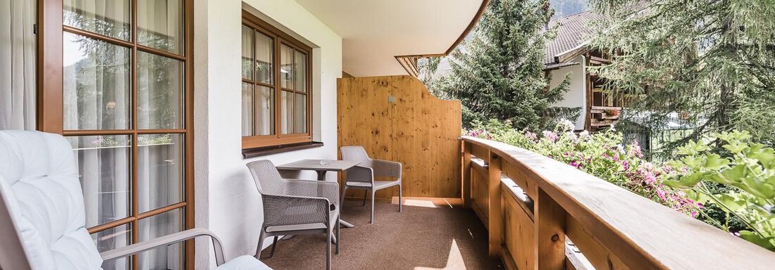 A cozy balcony with seating and a wooden railing. In the background, trees and a quiet environment are visible. - Andre Arnold - Boutique Hotel - Sölden