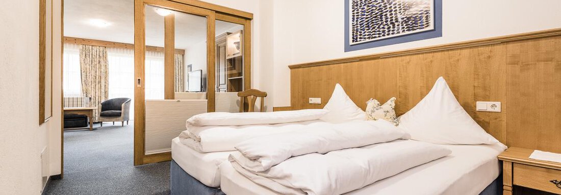 A modern bedroom with two beds and bright walls. In the background, a seating area and large windows can be seen. - Andre Arnold - Boutique Hotel - Sölden