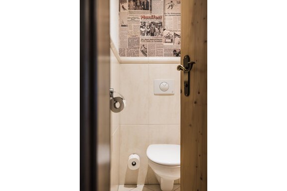 A small, modern bathroom with a toilet and a newspaper wall. The walls are designed in light colors, giving a clean impression. - Andre Arnold - Boutique Hotel - Sölden