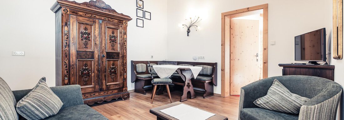 A cozy living space with a dark brown cabinet and a small table. The decor is stylish and the room has wooden beams on the ceiling. - Andre Arnold - Boutique Hotel - Sölden