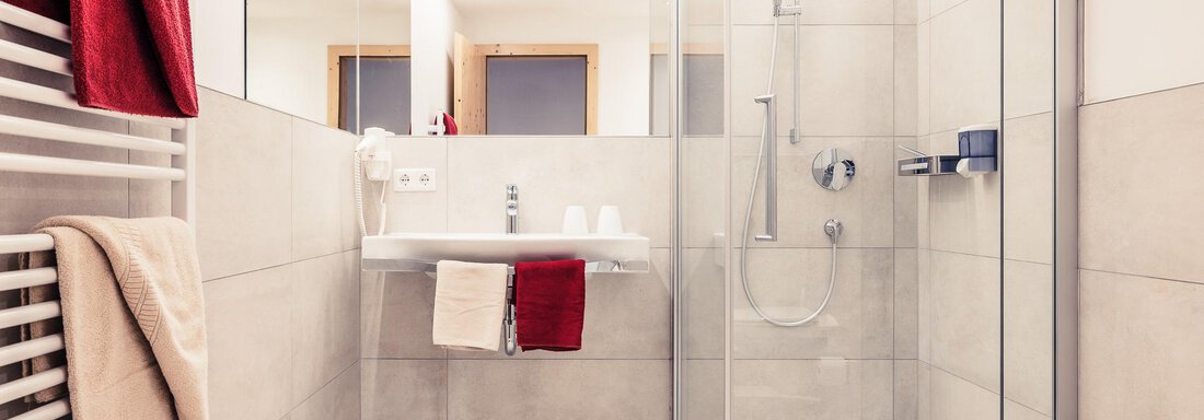 A modern bathroom with a glass shower and a sink. Red towels are decoratively hanging on the wall. - Andre Arnold - Boutique Hotel - Sölden