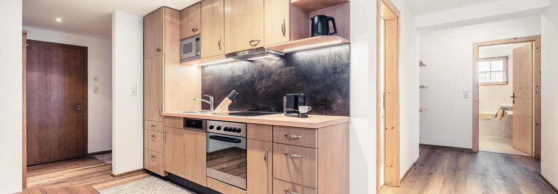 Modern kitchen unit with wooden furniture and modern appliances. Bright room with warm lighting and an inviting carpet. - Andre Arnold - Boutique Hotel - Sölden