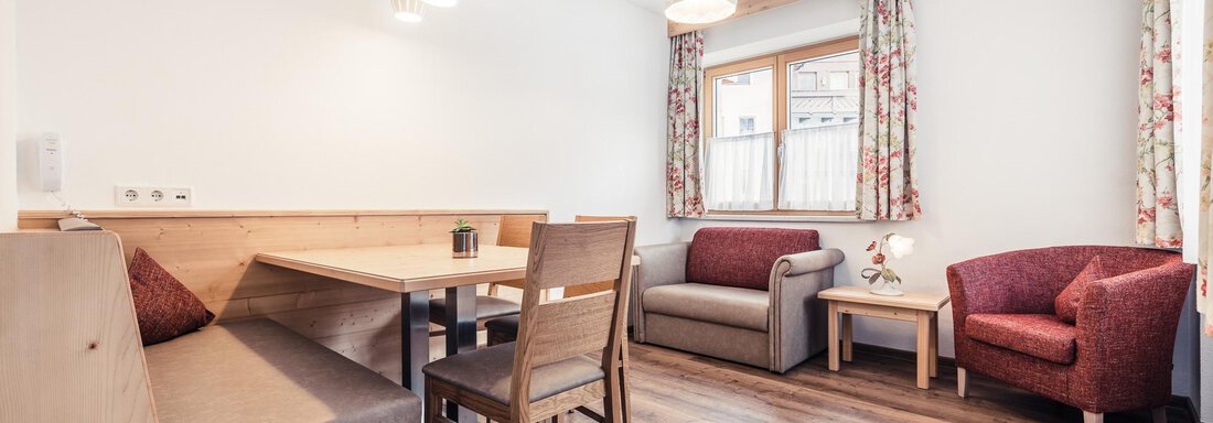 A bright and modern living room with a cozy sitting area and a dining table. Large windows provide plenty of daylight. - Andre Arnold - Boutique Hotel - Sölden