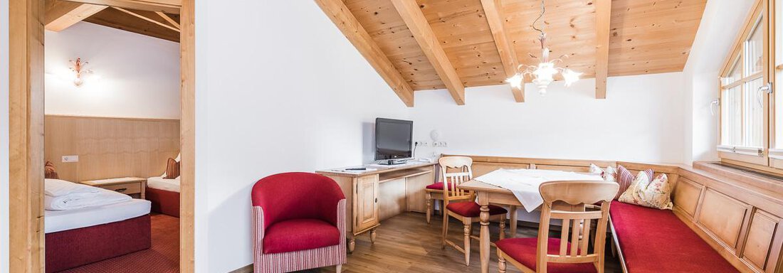 A bright and cozy room with wooden ceilings and modern design. There is a dining area with tables and chairs, as well as a separate bedroom. - Andre Arnold - Boutique Hotel - Sölden