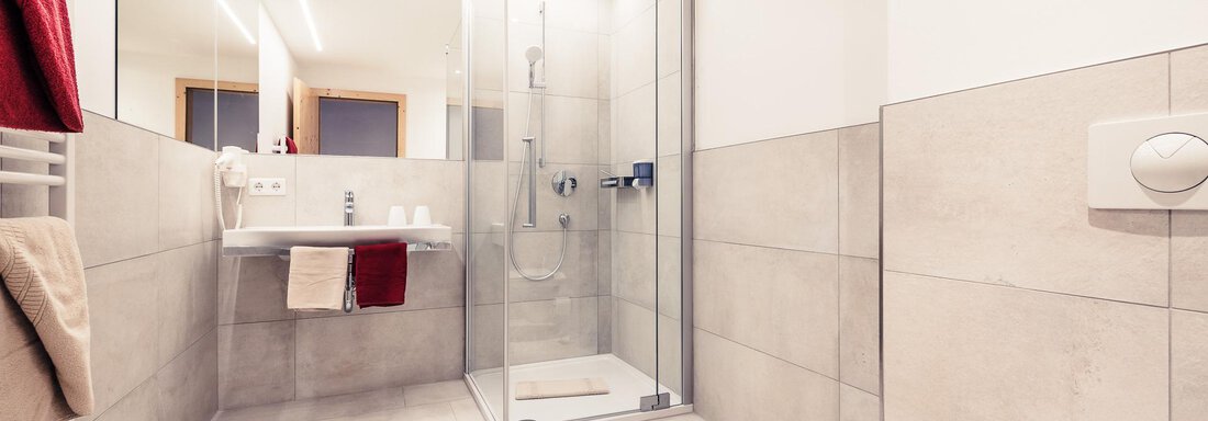 A modern bathroom with a spacious glass shower. Bright tiles and neutral colors create a fresh atmosphere. - Andre Arnold - Boutique Hotel - Sölden
