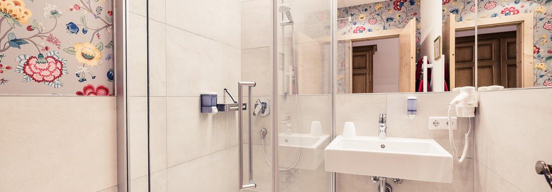 A modern bathroom with a shower cabin and a sink. The walls are decorated with a colorful floral pattern. - Andre Arnold - Boutique Hotel - Sölden