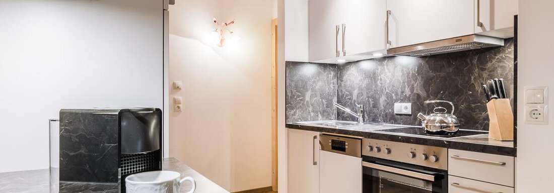 Modern kitchen with elegant gray countertops and bright cabinets. A coffee machine and a cup are on the counter. - Andre Arnold - Boutique Hotel - Sölden