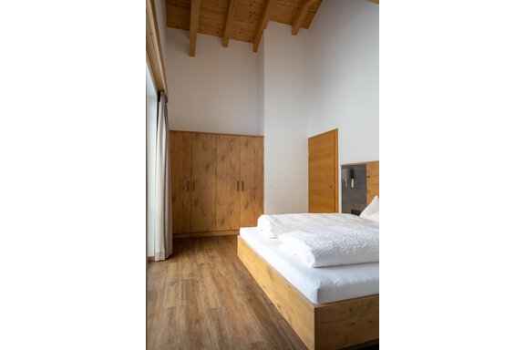 A modern bedroom with a wooden bed and minimalist furnishings. The walls are light and the floor is made of wood, creating a cozy atmosphere. - Anraitl Appartements Sölden - Sölden