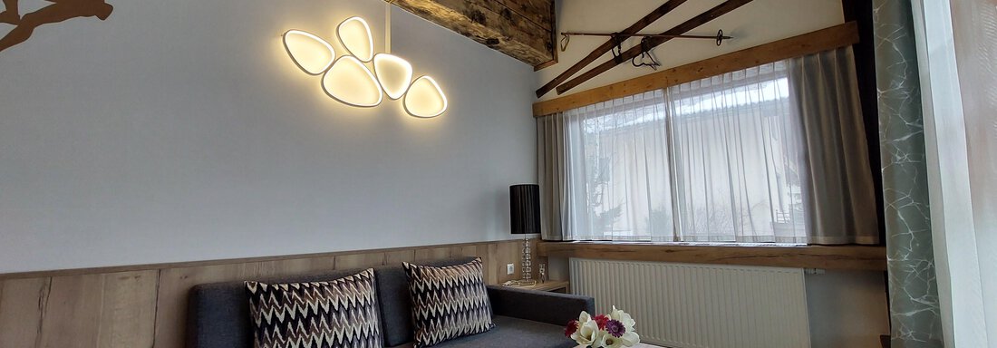 A cozy living room with a modern sofa and a wooden table. Old skis hang on the wall and the ceiling has rustic wooden beams. - Apart 77 - Sölden