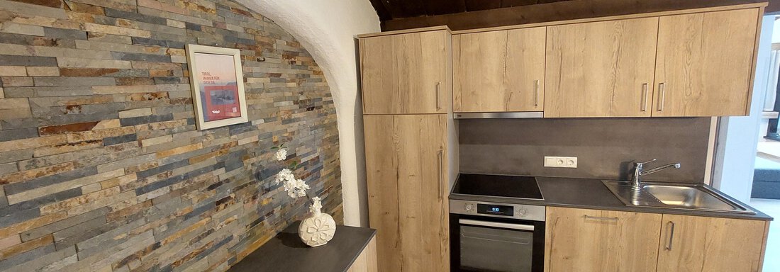A modern kitchen with wooden cabinets and a stone wall. There is a sink, a stove, and a refrigerator. - Apart 77 - Sölden