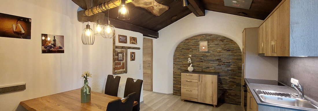 A cozy living space with wooden ceilings and a large dining table. The kitchen is modern and well-equipped, with a stone wall as a focal point. - Apart 77 - Sölden