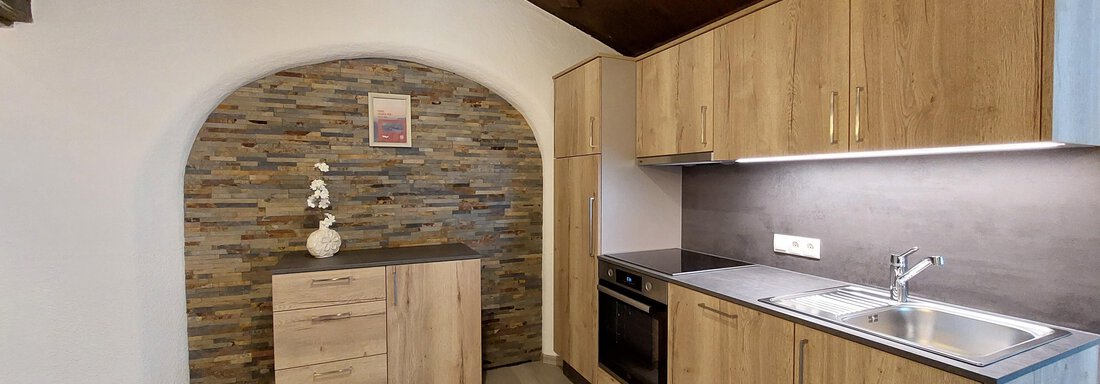 A modern kitchen with wooden cabinets and an elegant stone wall element. The rooms are designed to be bright and welcoming. - Apart 77 - Sölden
