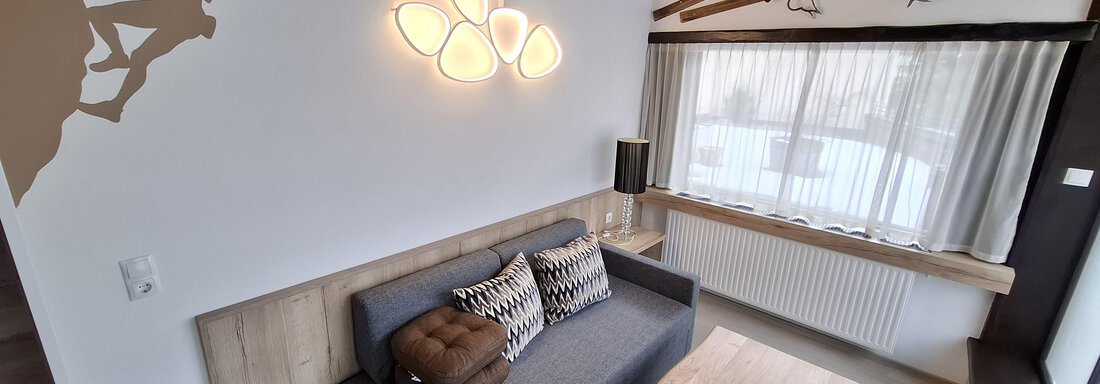 A modern living room with a gray sofa and a wooden ceiling. On the wall, there is a climber silhouette and two old skis decoratively mounted. - Apart 77 - Sölden