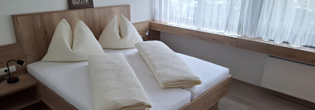 A cozy bedroom with a double bed and two decorative pillows. Large windows let in plenty of daylight. - Apart 77 - Sölden
