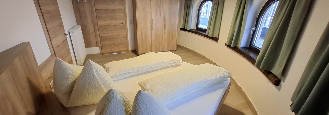 A cozy bedroom with two beds and light wooden furniture. Large windows let in plenty of daylight and the curtains are green. - Apart 77 - Sölden