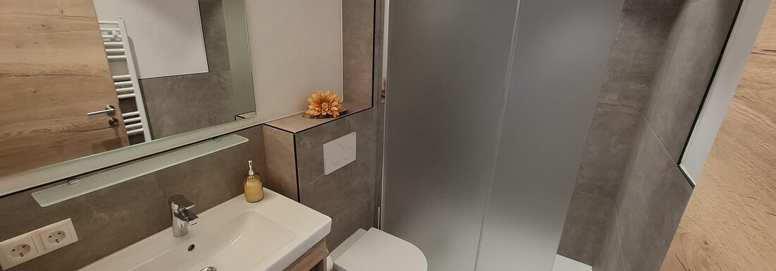 A modern bathroom with a shower and a sink. The walls are in neutral tones, and there are wooden elements for a cozy look. - Apart 77 - Sölden