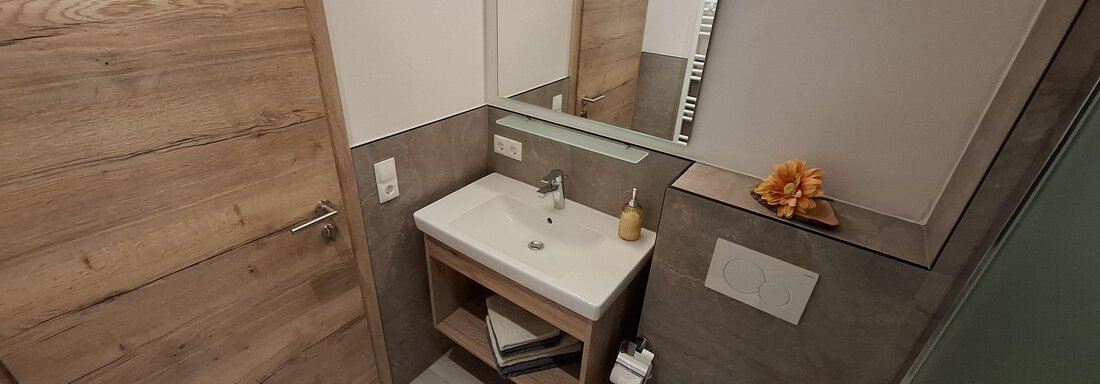 A modern bathroom with wood details and a sink. There is a mirror and a toilet, all kept in bright colors. - Apart 77 - Sölden