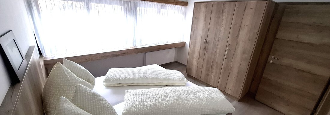 A modern bedroom with a large bed and bright, inviting colors. The walls are made of wood and there is plenty of natural light coming through the windows. - Apart 77 - Sölden