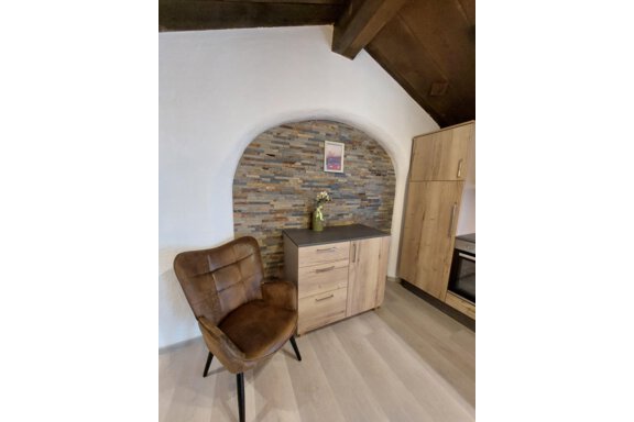 A cozy living area with a brown chair and a modern wooden dresser. In the background, a decorative stone wall can be seen. - Apart 77 - Sölden