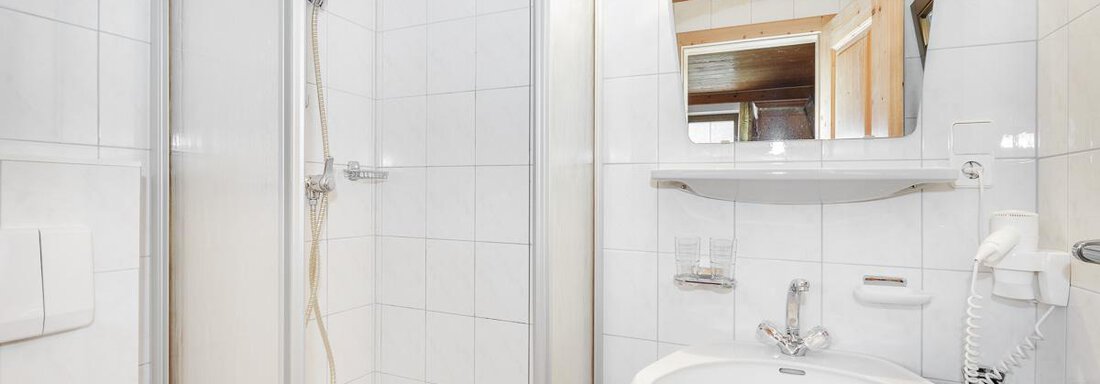 A modern bathroom with a shower and a sink. The walls are brightly tiled and there is a large mirror. - Apart Garni Enzian - Sölden