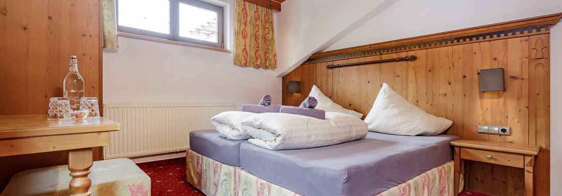 A cozy bedroom with a double bed and decorative pillows. The wood design and the carpet create a warm atmosphere. - Apart Garni Enzian - Sölden