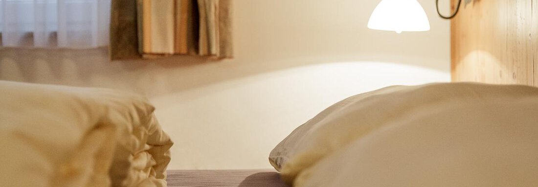 A cozy bedroom with two beds and soft pillows. A gentle lamp provides warm light. - Apart Garni Enzian - Sölden