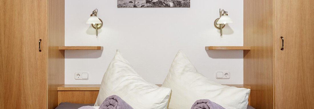 Doppelzimmer Basic | © RudiWyhlidal A cozy bedroom with two beds and a picture of mountains on the wall. Several rolled towels are placed on the beds. - Apart Garni Enzian - Sölden