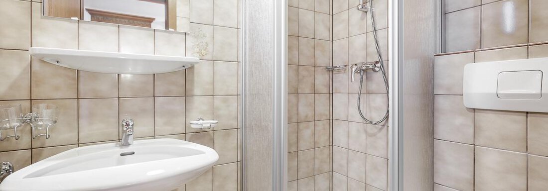 A modern bathroom with a shower, sink, and bright tiles. The decor is functional and clean. - Apart Garni Enzian - Sölden