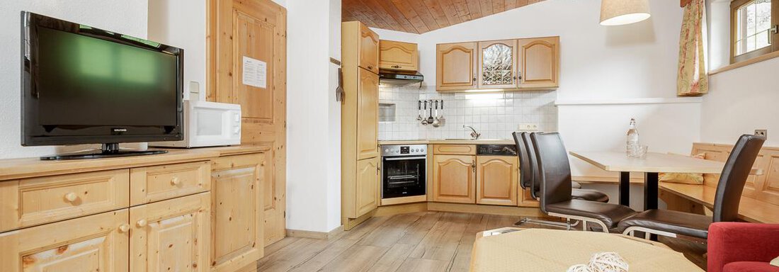 A cozy apartment with wooden furniture and an open kitchen corner. The living area is bright and inviting, perfect for relaxing. - Apart Garni Enzian - Sölden