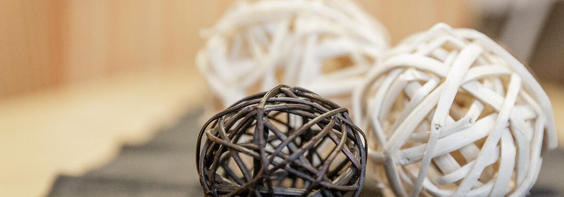 Three decorative rattan balls in different colors on a table. The black ball is in the foreground, while the white balls are in the background. - Apart Garni Enzian - Sölden