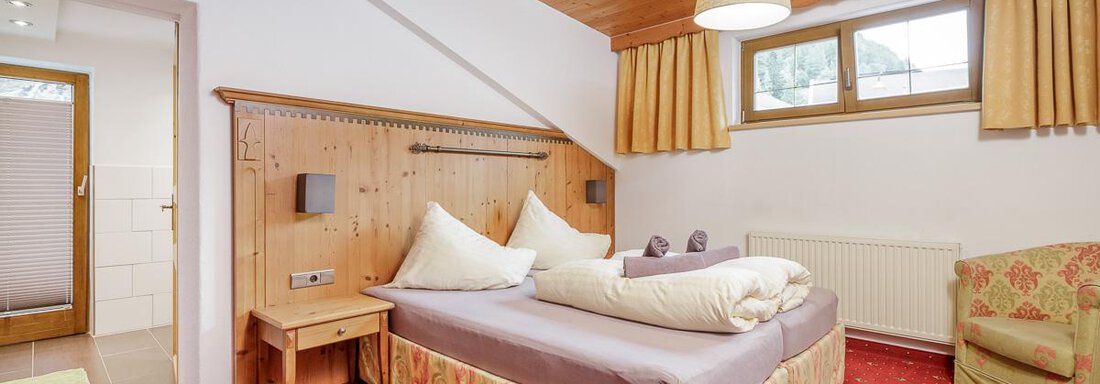 A cozy bedroom with a double bed and wooden furniture. The room has a red carpet and large windows with natural light. - Apart Garni Enzian - Sölden