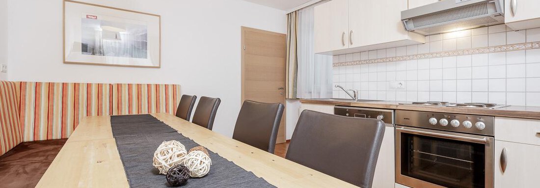 A modern kitchen and dining room with a large wooden table and six chairs. The kitchen is bright and well-equipped with cooking appliances. - Apart Garni Enzian - Sölden