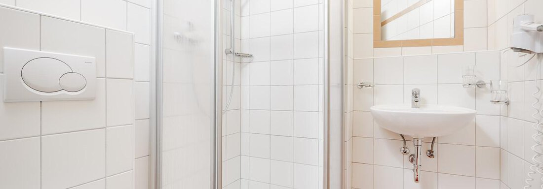 A modern bathroom with a shower cubicle and a sink. The walls are clad with white tiles and a red bath towel is lying on the floor. - Apart Garni Enzian - Sölden