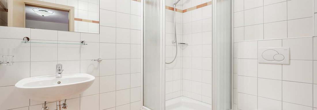 A modern bathroom with a shower cabin and a sink. The walls are brightly tiled and the floor has a geometric pattern. - Apart Garni Enzian - Sölden