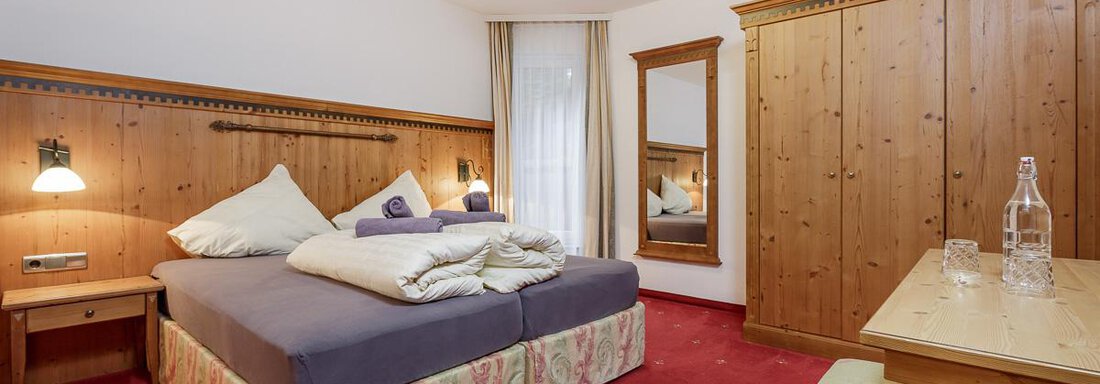 A cozy bedroom with wooden paneling and a large bed. The room is bright and inviting with a table and a mirror. - Apart Garni Enzian - Sölden