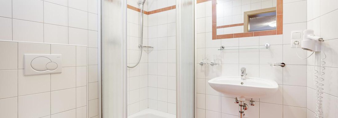 A modern bathroom with a shower, sink, and toilet. The walls are tiled and the floor is in warm tones. - Apart Garni Enzian - Sölden