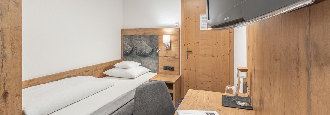 A cozy room with wooden furniture and a television. There is a single bed and a desk. - Apart Hotel Garni Alt Kaisers - Sölden