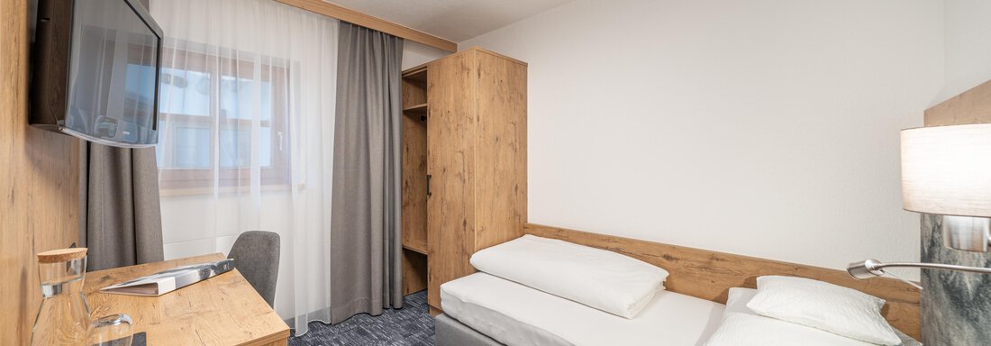 A simple, cozy, and modern room with wooden furniture. It features a single bed, a television, and carpet flooring. - Apart Hotel Garni Alt Kaisers - Sölden