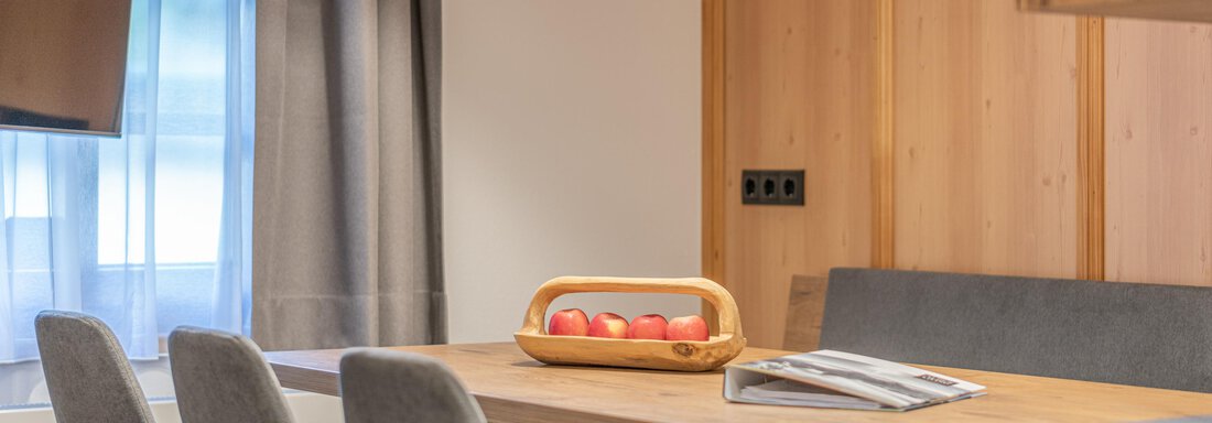 A modern kitchen with a wooden table and comfortable chairs. On the table sits a basket of red apples. - Apart Hotel Garni Alt Kaisers - Sölden