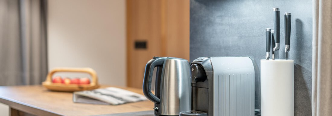 A modern kitchen unit with a kettle, a coffee machine, and kitchen knives. The wooden surface creates a warm atmosphere. - Apart Hotel Garni Alt Kaisers - Sölden