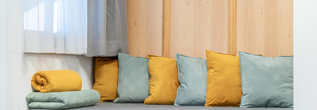 A cozy seating area with gray upholstery and colorful cushions. In the background, wooden paneling and curtains are visible. - Apart Hotel Garni Alt Kaisers - Sölden