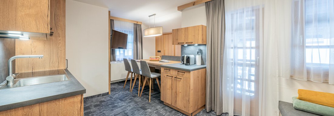 A modern kitchen with wooden furniture and a large window. The room is bright and inviting, with a dining area for four people. - Apart Hotel Garni Alt Kaisers - Sölden