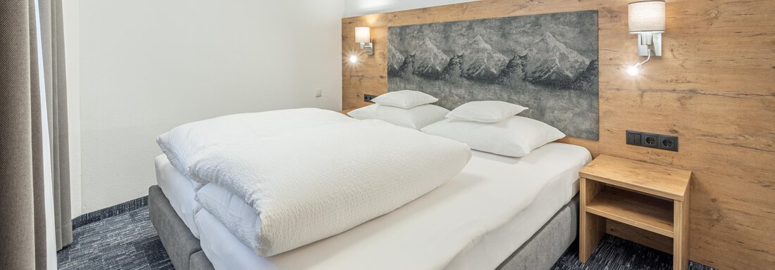 A modern bedroom with a large double bed and light-colored walls. Next to the bed is a nightstand. - Apart Hotel Garni Alt Kaisers - Sölden