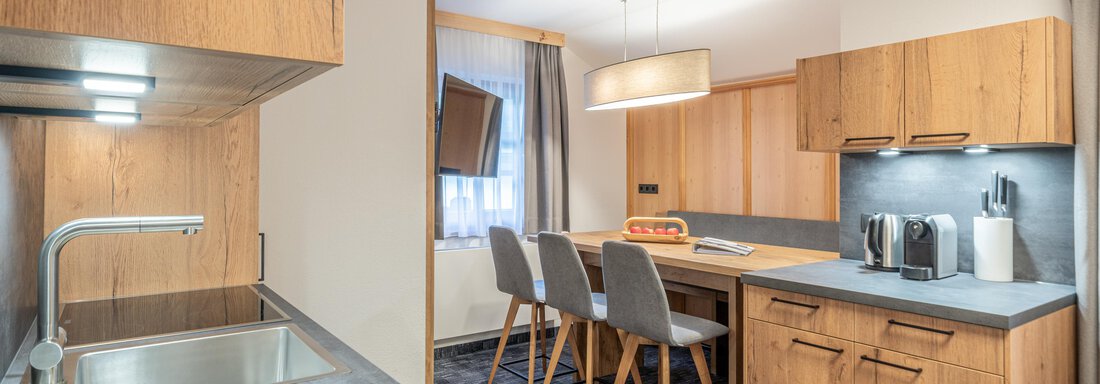 A modern kitchen with wooden cabinets and a dining table. The room is designed to be bright and friendly. - Apart Hotel Garni Alt Kaisers - Sölden