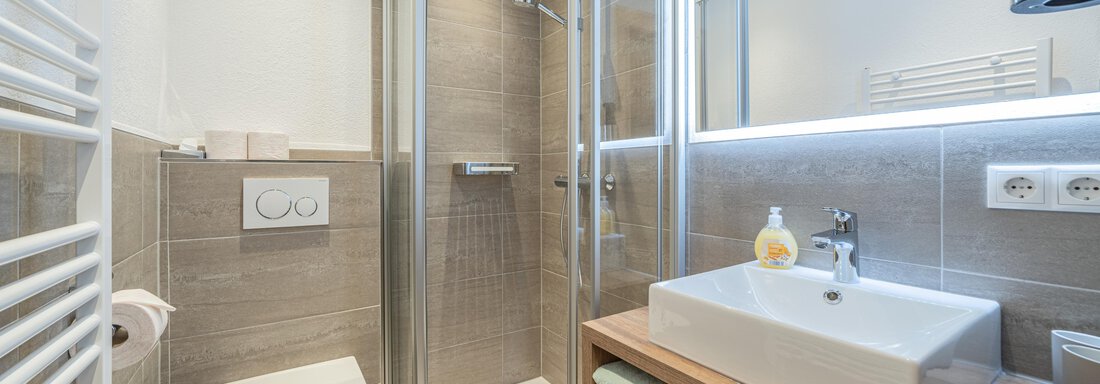 A modern bathroom with a shower cabin and an elegant sink. The walls are in neutral tones and there is ample storage space. - Apart Hotel Garni Alt Kaisers - Sölden