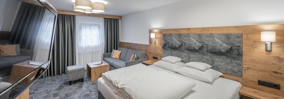 Doppelzimmer Tiefparterre - ohne Balkon | © JohannesBrunner (CC C) A modern hotel room with a large box spring bed and a cozy sitting area. The walls are designed with wood and neutral colors, and the light is pleasant. - Apart Hotel Garni Alt Kaisers - Sölden